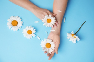 Woman with beautiful chamomile flowers on color background, top view