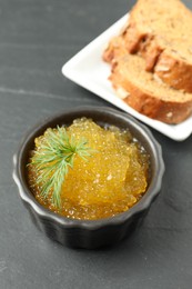 Photo of Fresh pike caviar in bowl and bread on black table