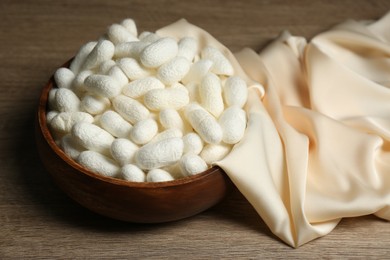 White cocoons with bowl and silk fabric on wooden table, closeup