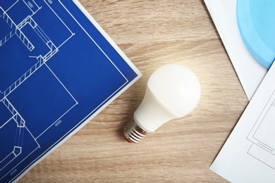Photo of Lamp bulb and blueprint on wooden table, top view