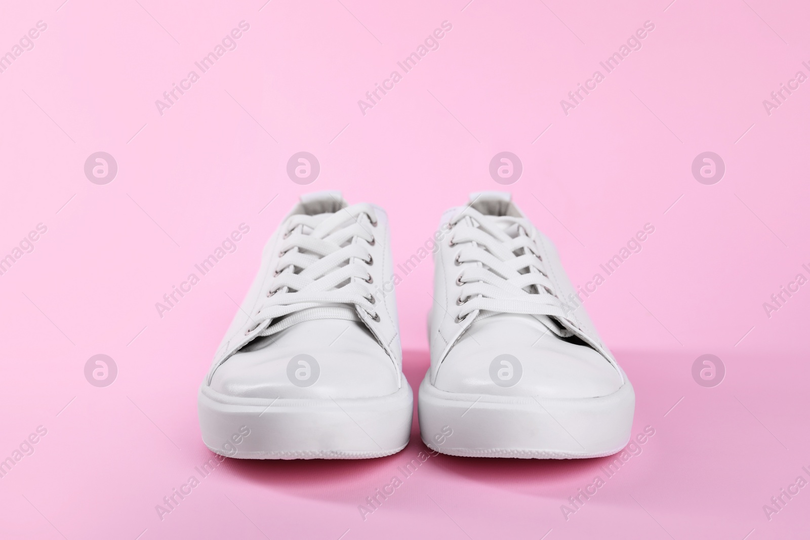 Photo of Pair of stylish white sneakers on pink background