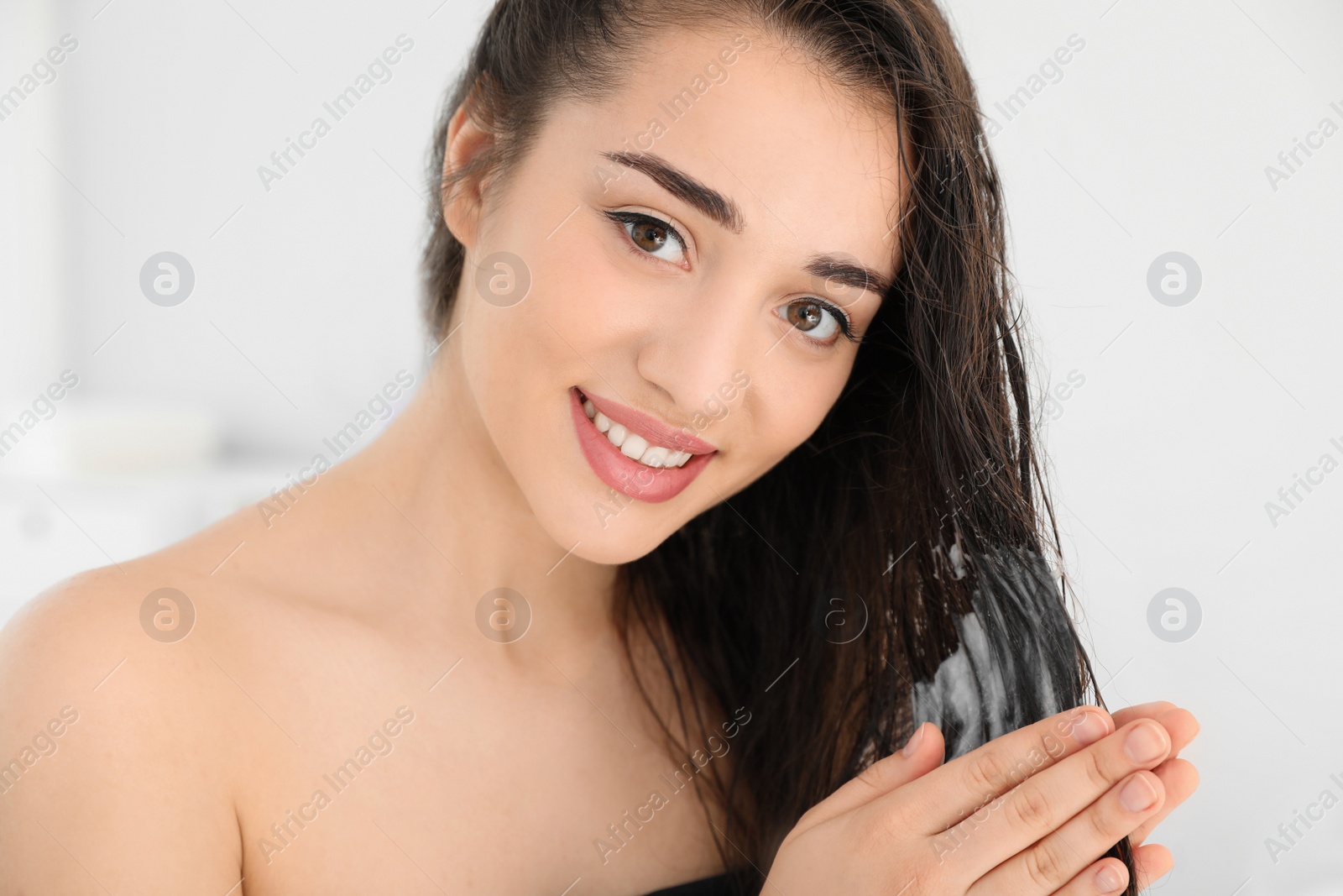 Photo of Beautiful young woman applying hair conditioner in bathroom