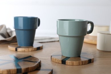 Photo of Mugs of hot drink with stylish cup coasters on wooden table