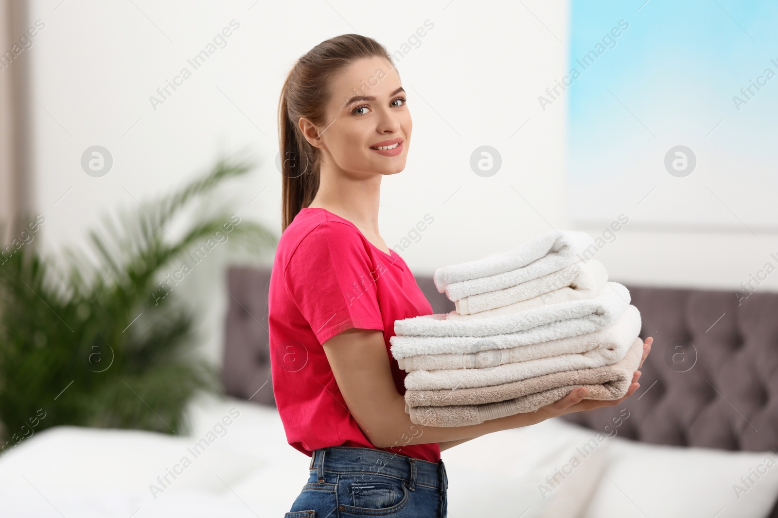 Photo of Woman holding folded clean towels in bedroom. Laundry day