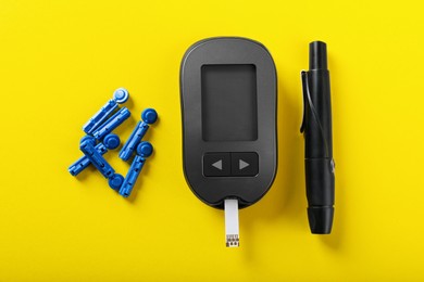 Photo of Digital glucometer with test strip, lancets and pen on yellow background, flat lay. Diabetes control