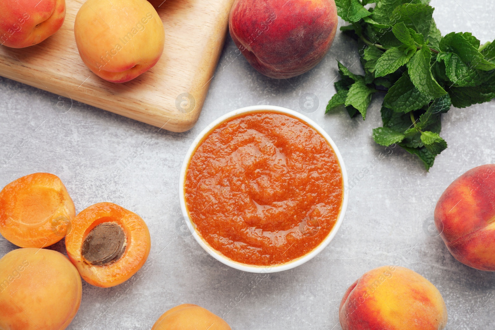 Photo of Apricot puree in bowl and fresh fruits on light grey table, flat lay