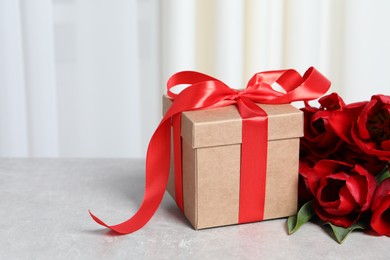 Photo of Beautiful gift box with bow and red tulip flowers on light table, closeup. Space for text