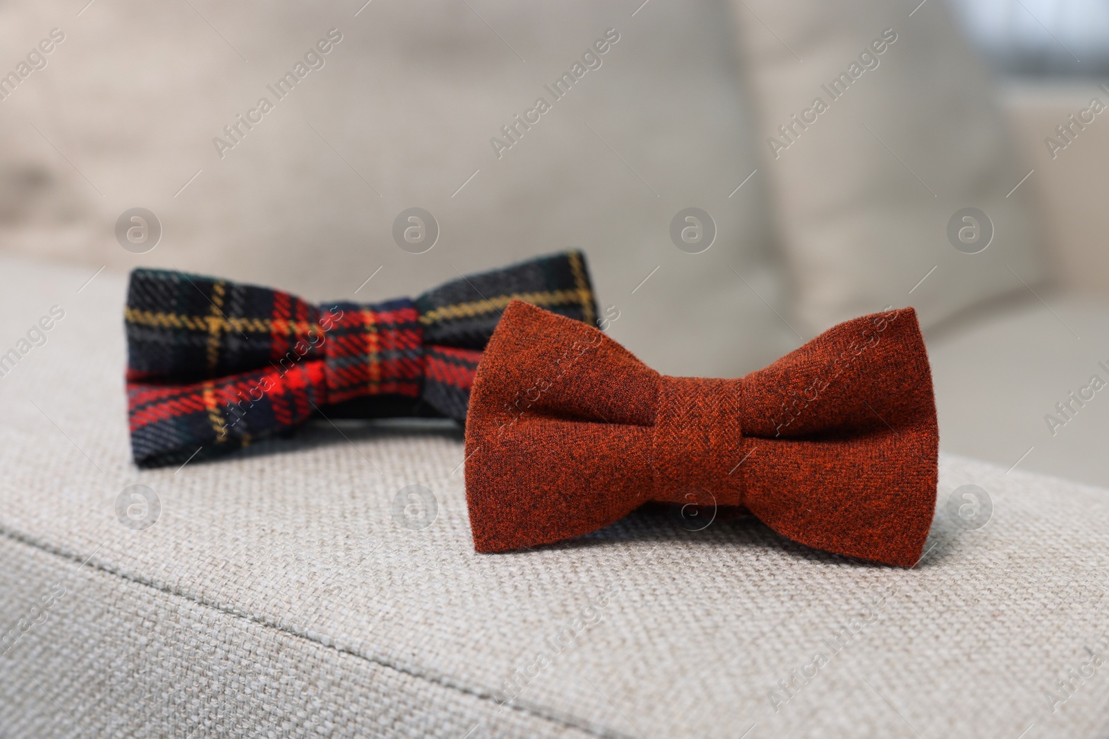 Photo of Stylish color bow ties on light grey sofa, closeup