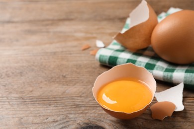 Photo of Cracked raw chicken egg with yolk on wooden table, closeup. Space for text