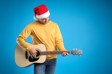 Photo of Man in Santa hat playing acoustic guitar on light blue background, space for text. Christmas music