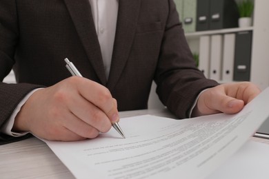 Man signing document at wooden table, closeup