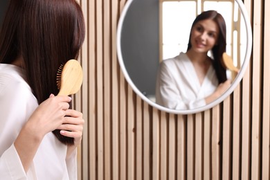 Photo of Beautiful woman brushing her hair near mirror in room, space for text