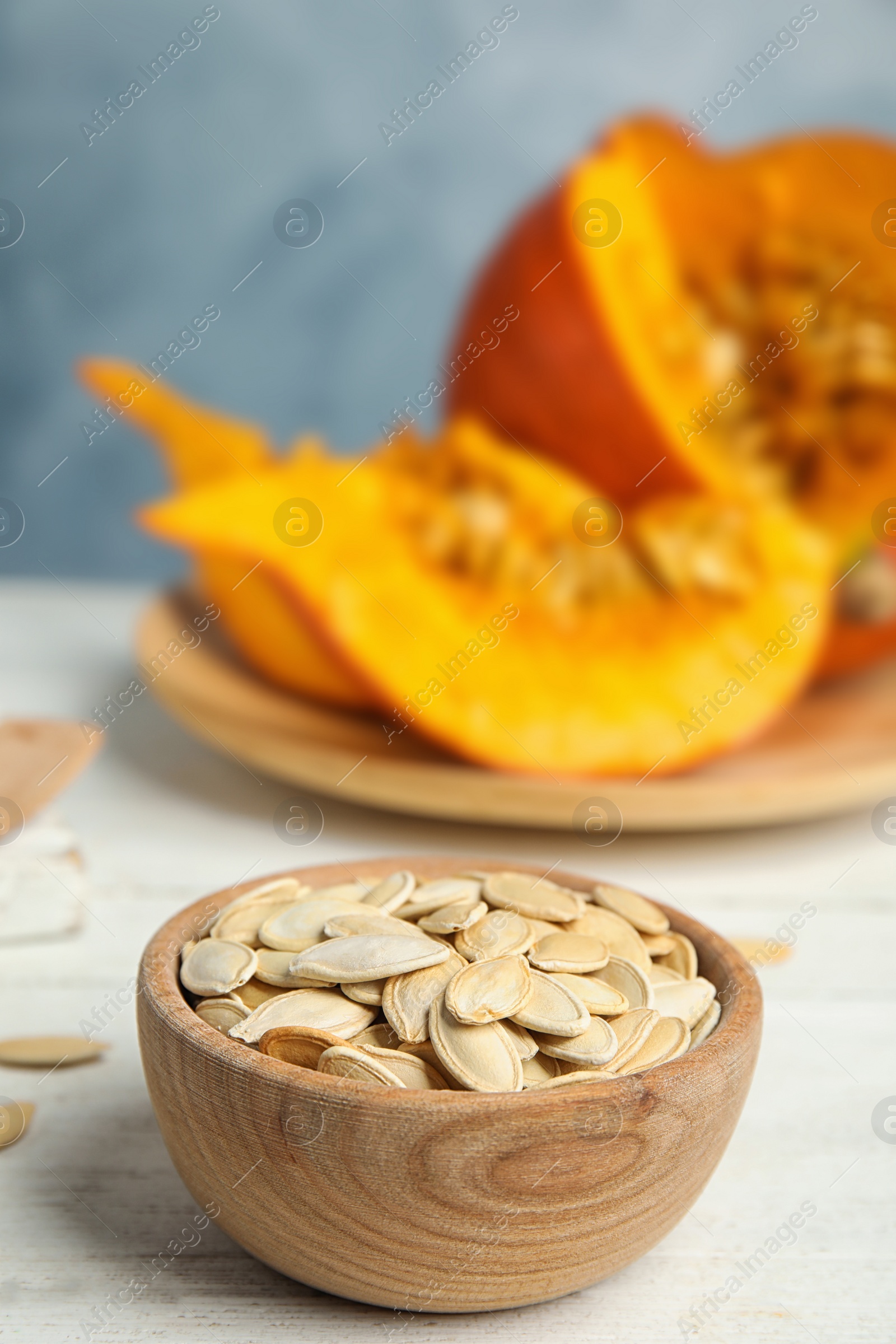 Photo of Bowl of raw pumpkin seeds on white wooden table