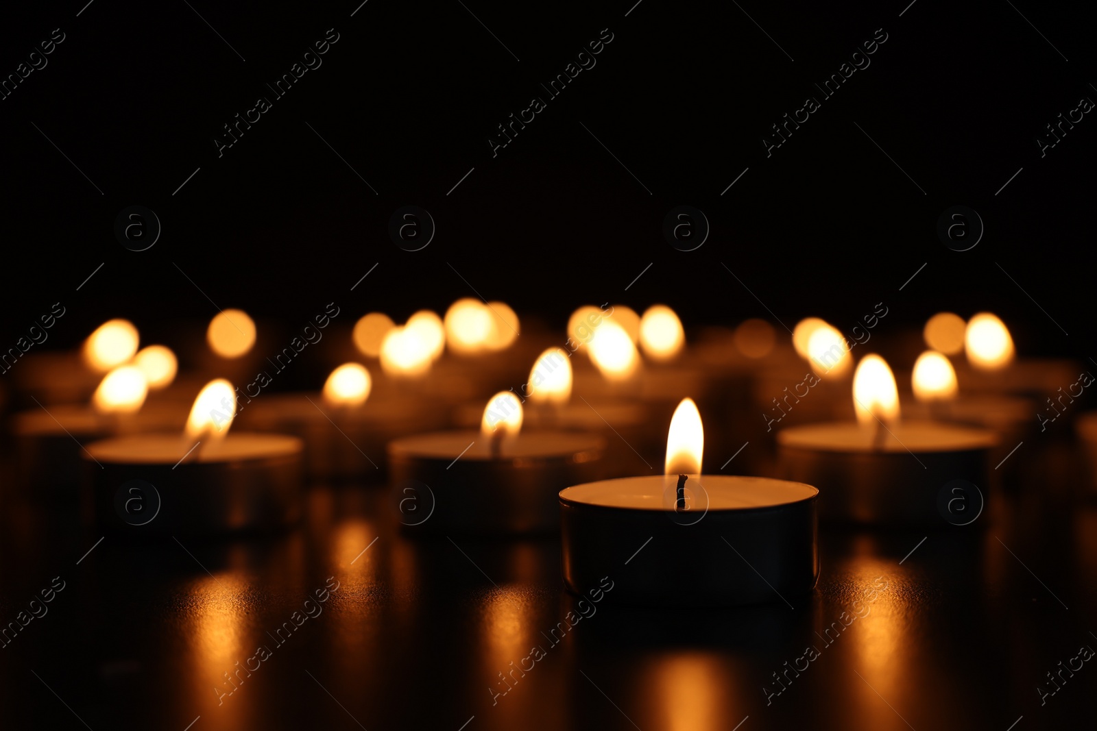Photo of Burning candles on dark surface against black background, closeup