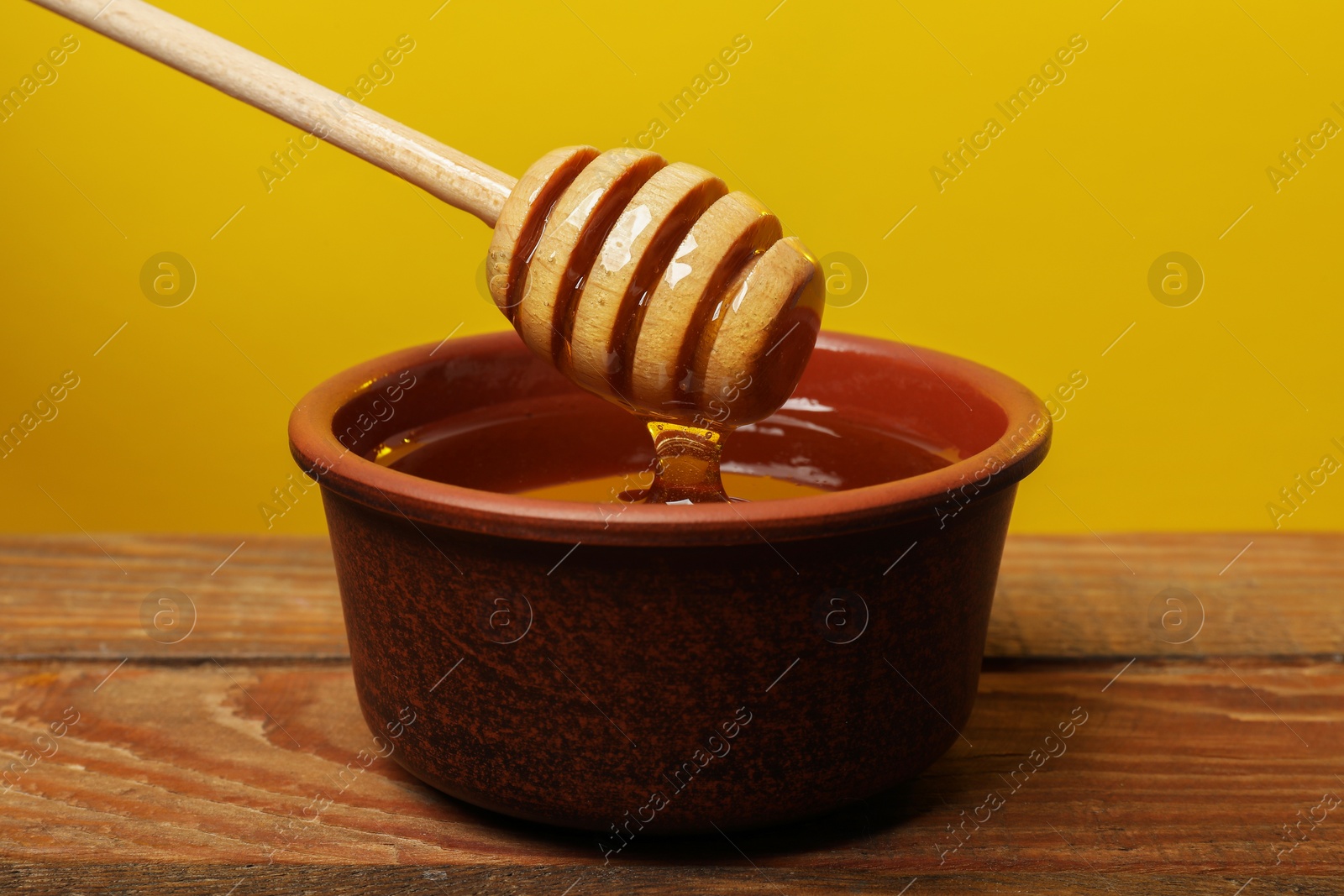 Photo of Pouring honey from dipper into bowl at wooden table against golden background