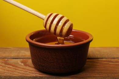 Photo of Pouring honey from dipper into bowl at wooden table against golden background