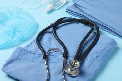Photo of Medical uniform, stethoscope and antiseptic on light blue background, closeup view