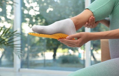 Photo of Woman fitting orthopedic insole indoors, closeup. Foot care