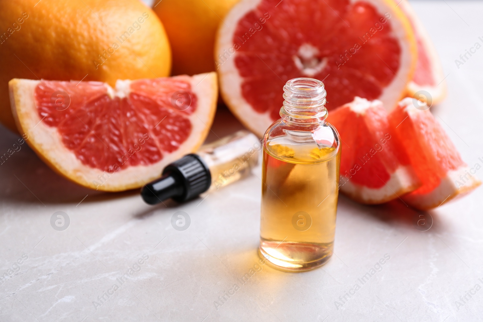 Photo of Bottle of essential oil and grapefruits on grey table, space for text