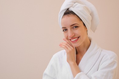 Beautiful young woman with hair wrapped in towel after washing on beige background. Space for text