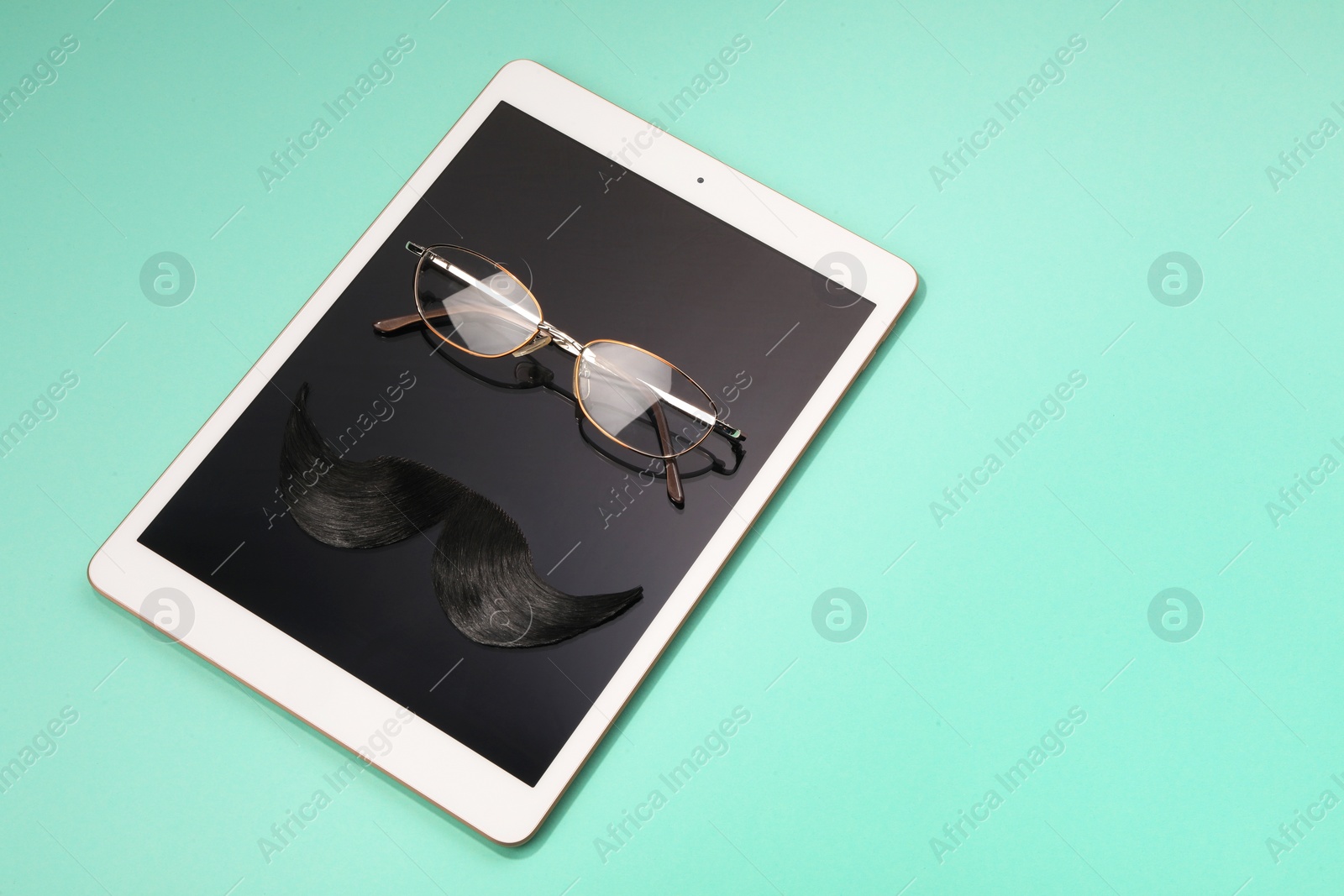 Photo of Artificial moustache, tablet and glasses on turquoise background, above view. Space for text