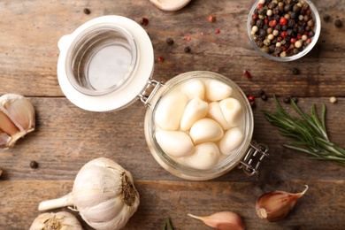 Photo of Preserved garlic in glass jar on wooden table, flat lay