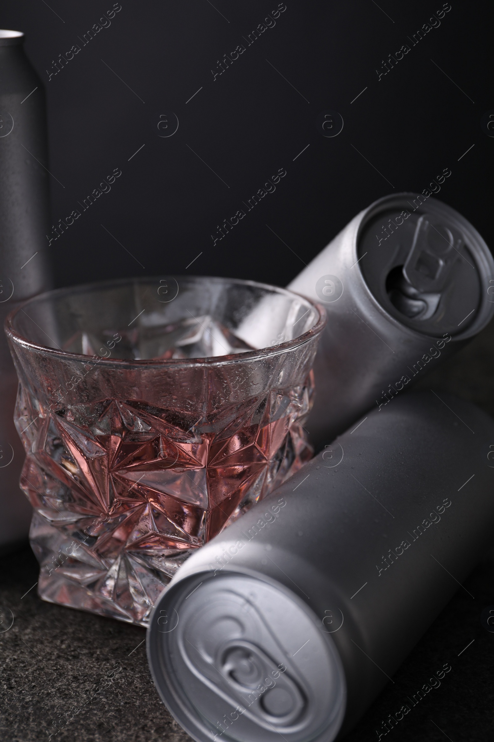 Photo of Energy drink in glass and aluminium cans on grey table, closeup