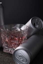 Photo of Energy drink in glass and aluminium cans on grey table, closeup