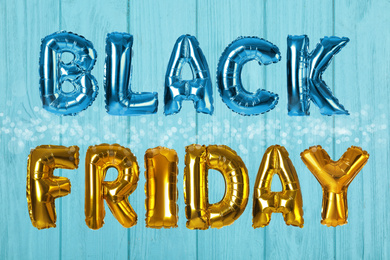 Image of Phrase BLACK FRIDAY made of foil balloon letters on light blue wooden background