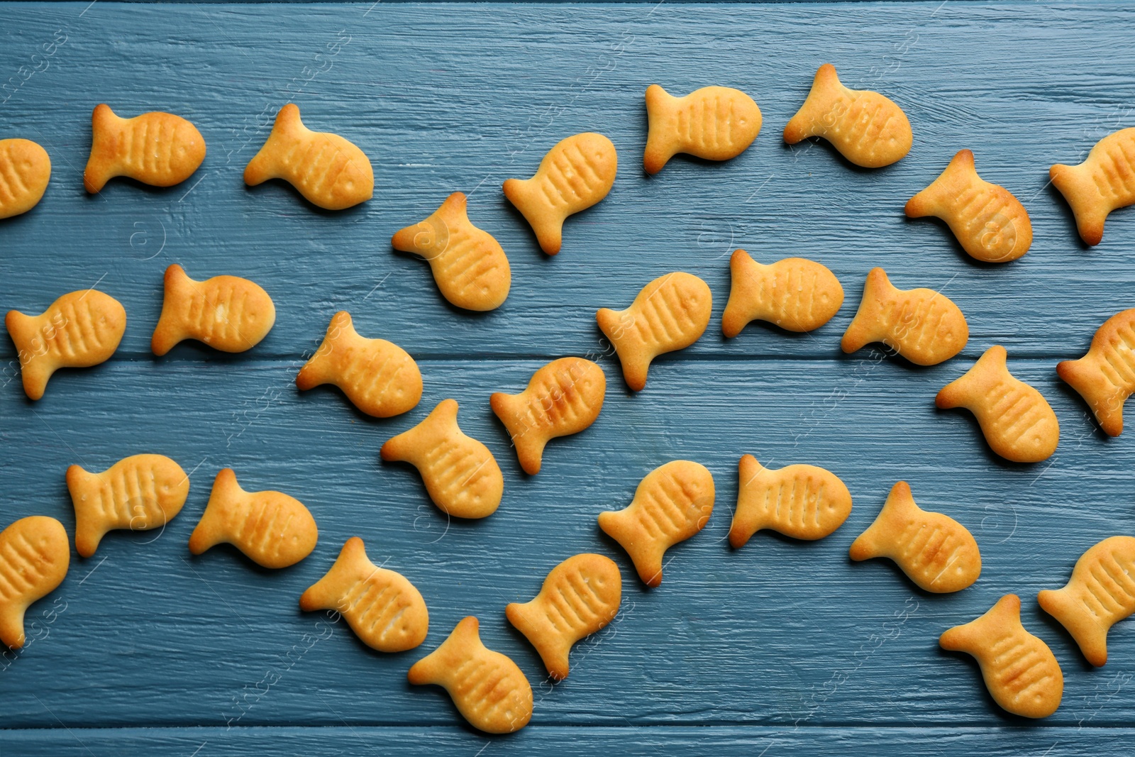 Photo of Delicious goldfish crackers on blue wooden table, flat lay