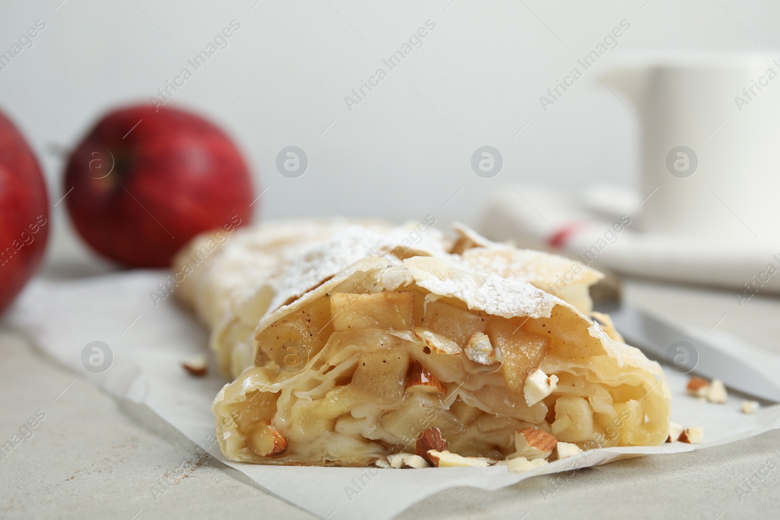 Photo of Delicious apple strudel with almonds and powdered sugar on light grey table, closeup. Space for text