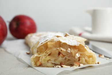 Photo of Delicious apple strudel with almonds and powdered sugar on light grey table, closeup. Space for text