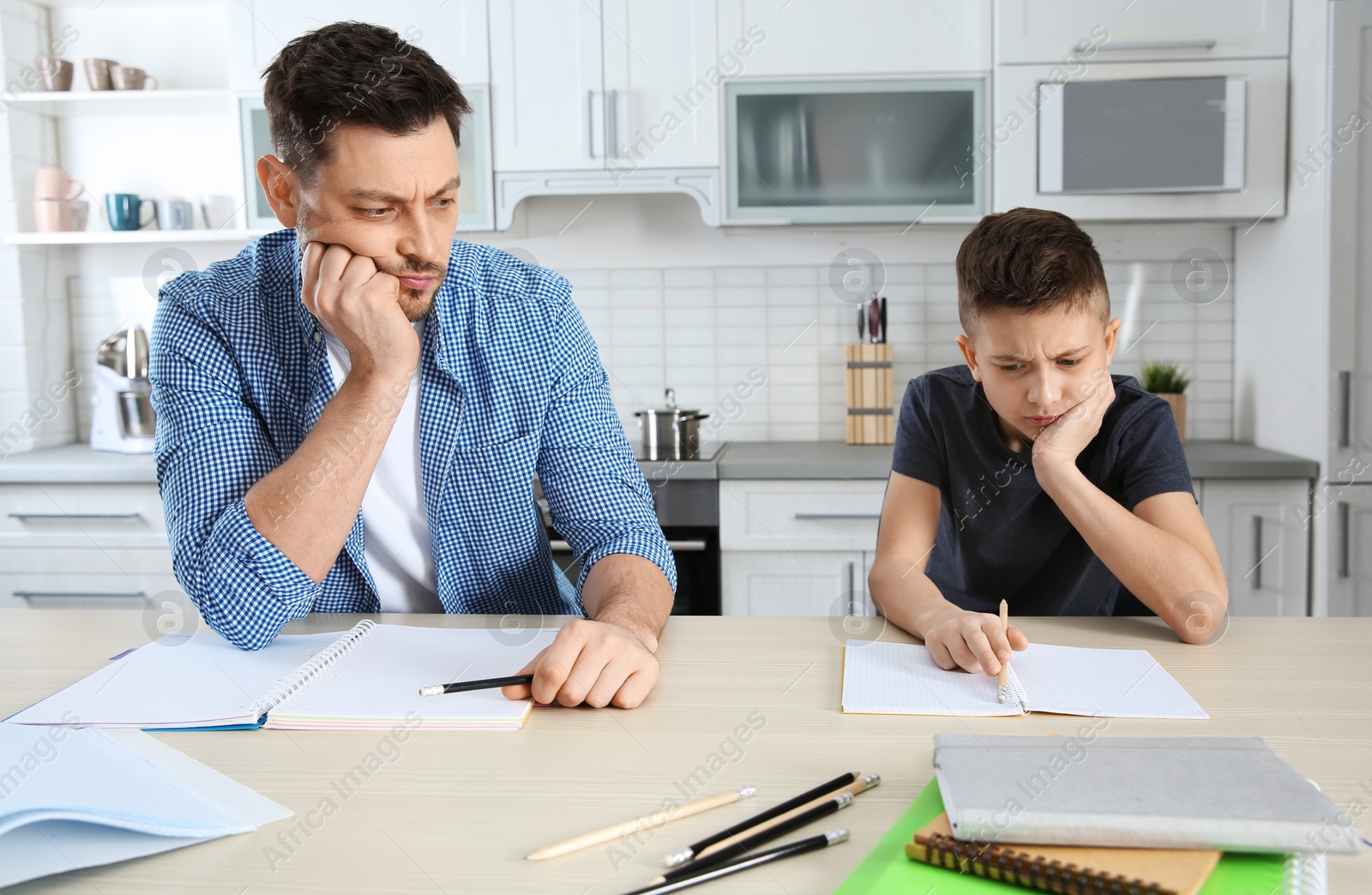 Photo of Dad helping his son with difficult homework assignment in kitchen