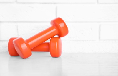 Stylish dumbbells on table against brick wall, space for text. Home fitness