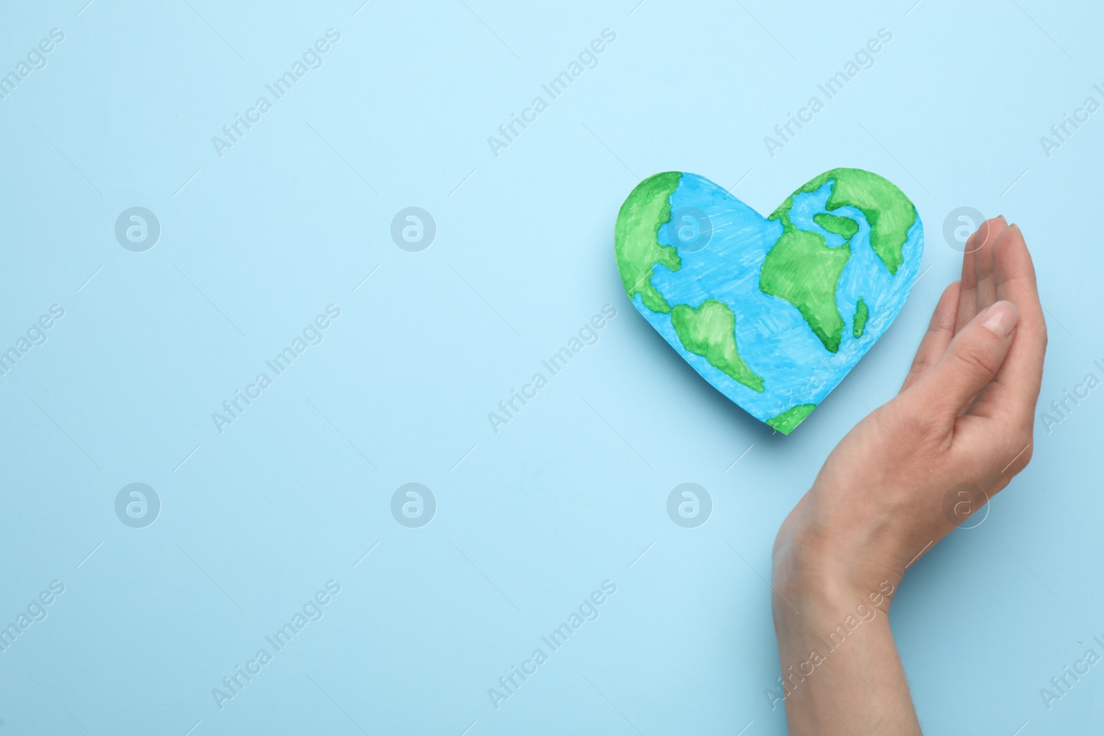 Photo of Woman and heart shaped model of planet on light blue background, top view with space for text. Earth Day