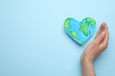 Photo of Woman and heart shaped model of planet on light blue background, top view with space for text. Earth Day