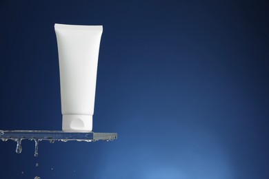 Photo of Moisturizing cream in tube on glass with water drops against blue background. Space for text