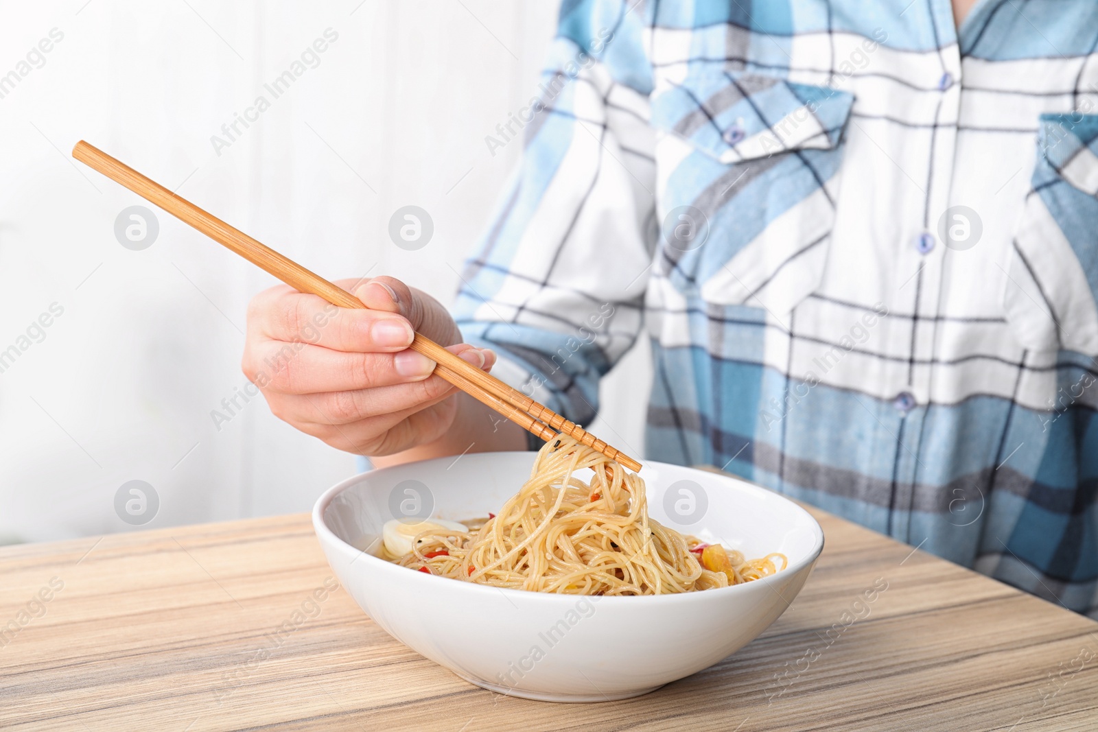 Photo of Woman eating cooked Asian noodles with chopsticks at table, closeup