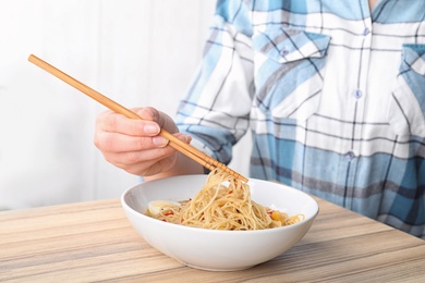 Photo of Woman eating cooked Asian noodles with chopsticks at table, closeup