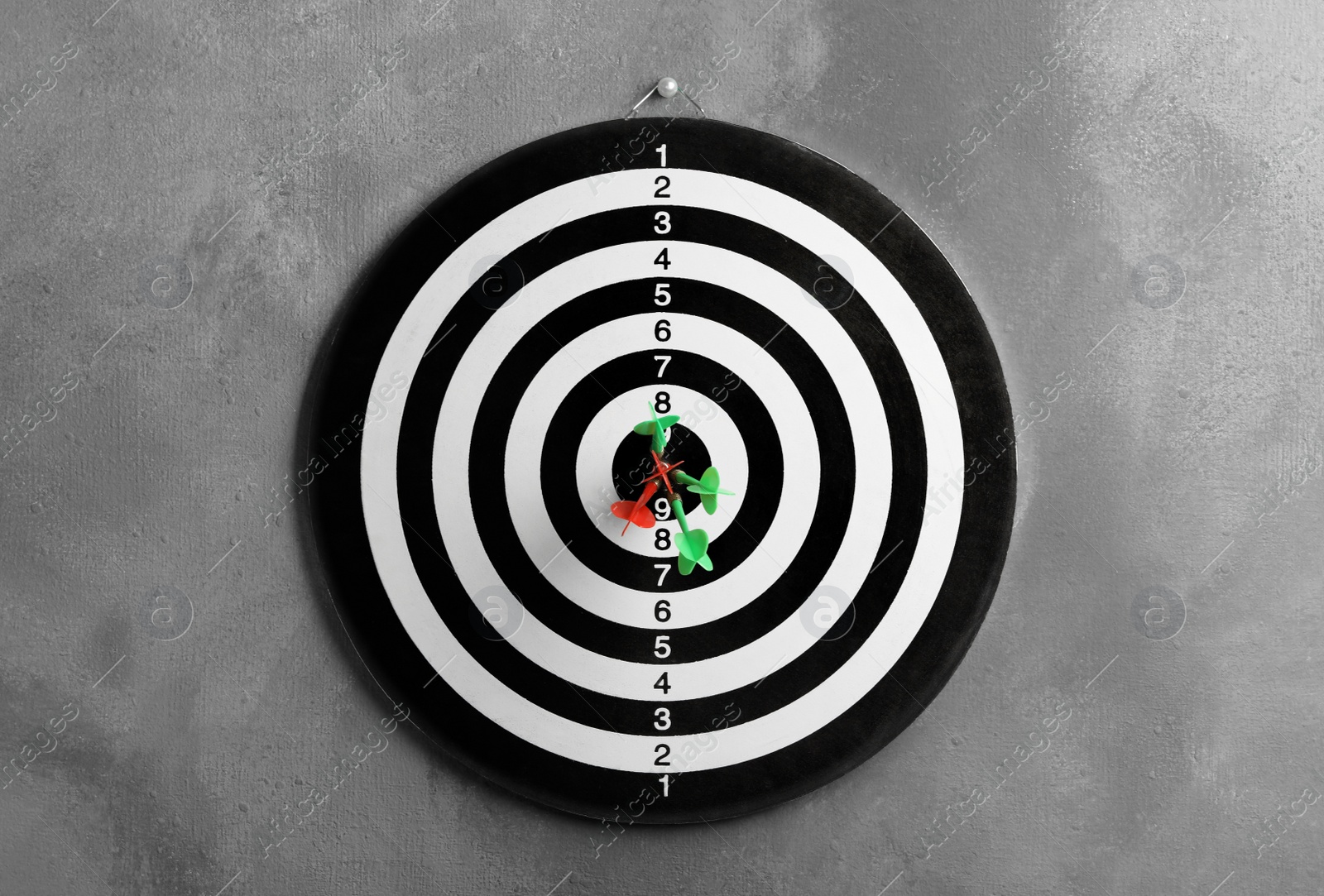 Photo of Dart board with arrows hitting target on grey wall