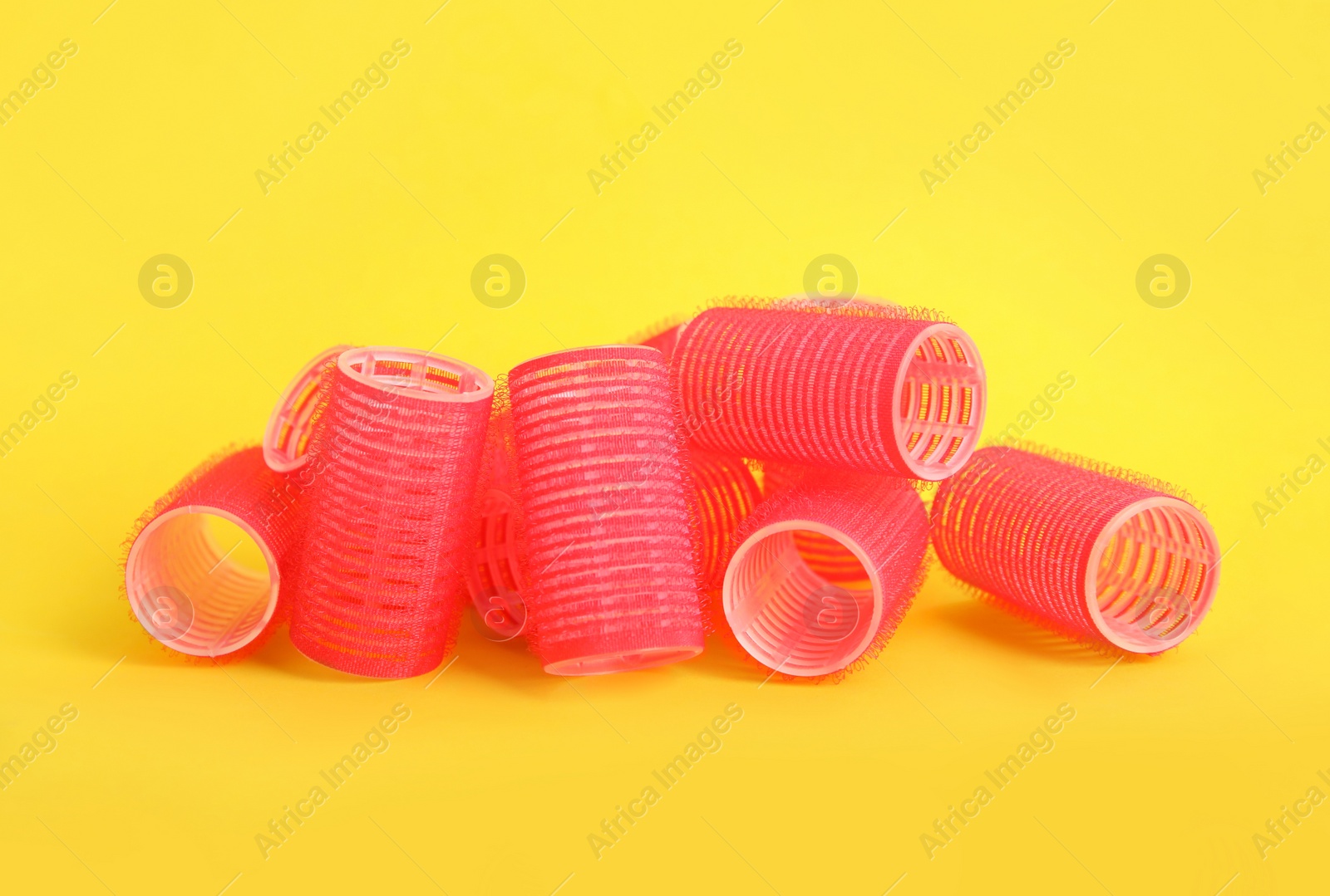 Photo of Many red hair curlers on yellow background