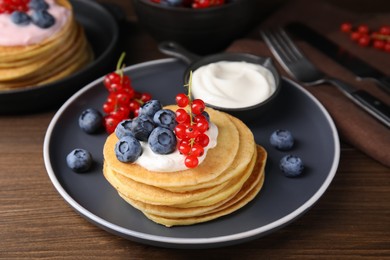 Photo of Tasty pancakes with natural yogurt, blueberries and red currants on wooden table