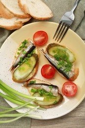 Photo of Delicious sandwiches with sprats, pickled cucumber and green onion served with tomatoes on wooden table, flat lay