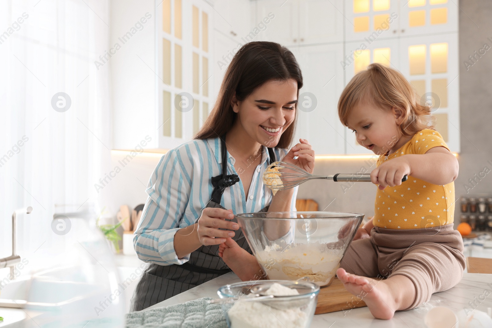 Photo of Mother and her little daughter cooking dough together in kitchen