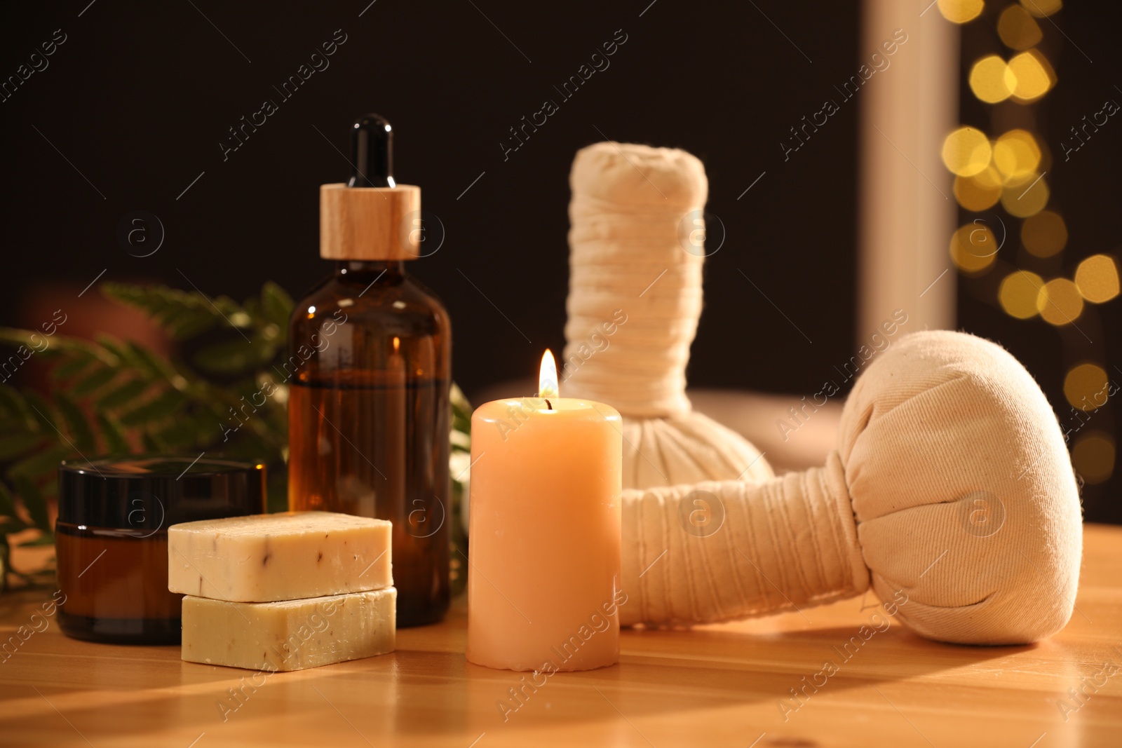 Photo of Spa composition. Cosmetic products, herbal bags and burning candle on wooden table