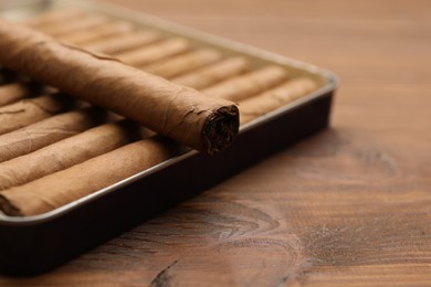 Photo of Many cigars in box on wooden table, closeup