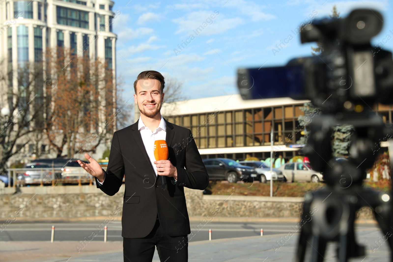 Photo of Young male journalist with microphone working on city street