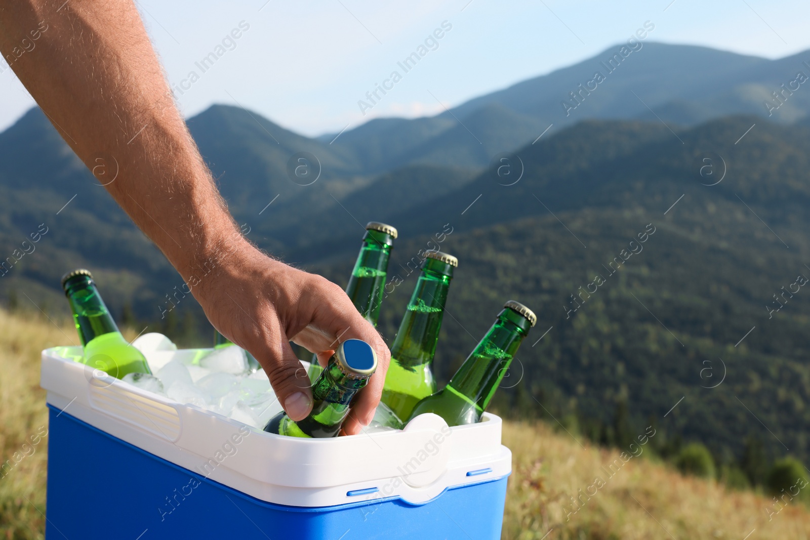 Photo of Man taking bottle of beer from cool box in mountains, closeup