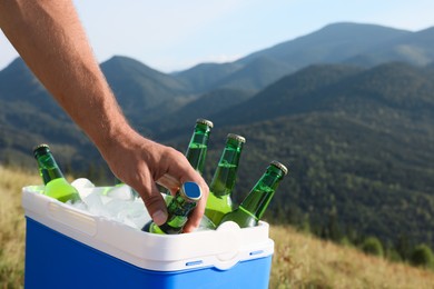 Man taking bottle of beer from cool box in mountains, closeup