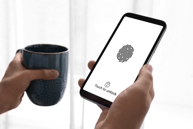 Image of Woman holding smartphone with fingerprint sensor indoors, closeup. Digital identity